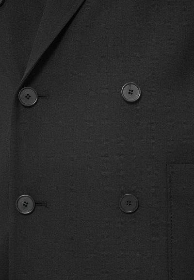 Μαύρη διπλή σαλοπέτα με μεγάλες μαύρες κουμπιά, με λείο υλικό και έντονα πέτα. Περιλαμβάνει λεπτομέρεια πλαϊνής τσέπης.