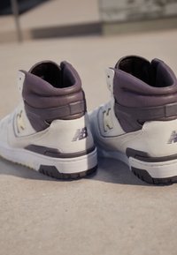 High-Top-Sneaker in einem beigen und dunkellila Farbschema, aus strukturiertem Leder, mit Logo-Akzenten und einem gepolsterten Schaft.