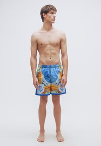 Μαγιό σορτς με πολύχρωμο σχέδιο παραλίας. Μπλε βασικό χρώμα, ελαστική μέση και άνετη εφαρμογή. Ελαφρύ ύφασμα, κοντό μήκος.
