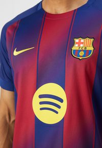 Tricoul FC Barcelona prezintă dungi verticale roșii și albastre, logo-ul Nike în aur și un logo mare Spotify galben în centru.
