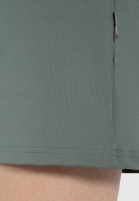 Kortärmad, mörkgrön topp gjord av mjukt tyg. Har en rak nederkant, enkelt design och en liten logotags på sömmen.