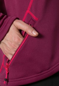 Morottröd sportjacka med rosa dragkedjor och sömmar. Har en sidoficka med dragkedja och ett mjukt, texturerat tyg.