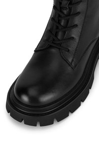 Czarny skórzany botek za kostkę z teksturowaną powierzchnią, okrągłym noskiem oraz grubą czarną gumową podeszwą z wyraźnym bieżnikiem i sznurowaniem z przodu.