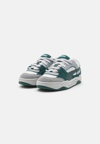 Sneaker Puma con un design teal e bianco, realizzate con materiali in suede e mesh, lacci, linguetta imbottita e suola in gomma testurizzata.