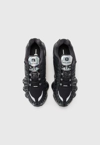 Sorte Nike Shox-sneakers med mesh-overdele, gummisåler, sølvaccenter og fremtrædende støddæmpningselementer. Har snørebånd og logo-detajer.