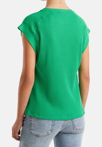 Zelený žebrovaný top s krátkým rukávem a kulatým výstřihem, s volným střihem a texturovaným povrchem. Zadní pohled ukazuje švy na ramenou a lem.