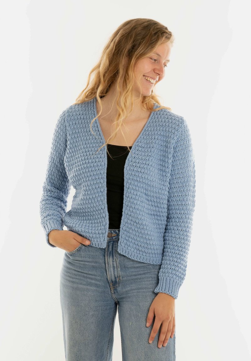 Lichtblauwe gebreide cardigan met een textuurpatroon, open voorkant, lange mouwen en geribbelde manchetten, gecombineerd met een zwarte top en lichte jeans.