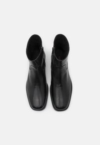 Bottes chevilles en cuir noir à texture lisse, bout pointu, fermeture éclair latérale et petit talon. Design épuré avec des détails minimalistes.