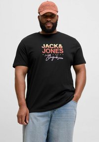 Juodas trumpomis rankovėmis marškinėliai su spalvingu logotipo spaudiniu, derinami su šviesiai mėlynomis džinsinėmis šortais ir rožine kepure su tekstūruotu užrašu.