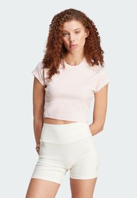 Light pink cropped t-shirt with short sleeves, featuring a subtle logo. Paired with high-waisted, ribbed white shorts.