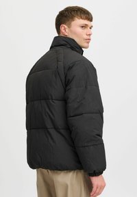 Sort puffjakke med quiltet design, høj krave, elastiske ærmer og en let tekstur, set fra ryggen.