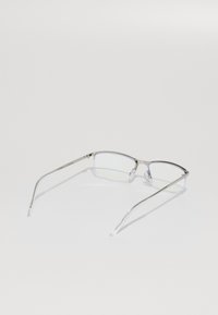 Óculos com armação metálica e lentes retangulares, apresentando pontas de orelha transparentes e um acabamento prateado, sobre um fundo branco.