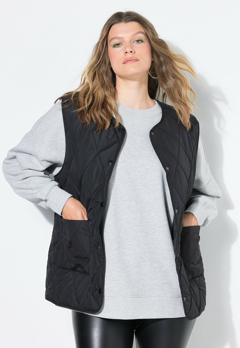 Schwarze gesteppte Weste mit Druckknöpfen und Seitentaschen, getragen über einem grauen Sweatshirt, mit einem lässigen Design und lockerer Passform.