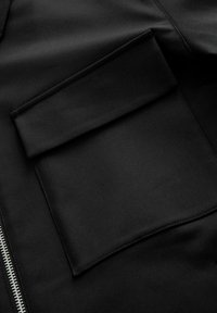 Veste noire avec une poche plate, texture lisse et fermeture éclair métallique. Design simple mettant l'accent sur la fonctionnalité.