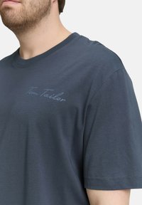 Donkerblauwe katoenen t-shirt met korte mouwen, met een subtiele lichtblauwe "Tom Tailor" logo op de borst. Gladde texture en reguliere pasvorm.