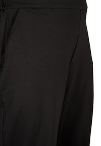 Jogging en tissu noir avec une texture lisse, présentant une coupe décontractée et des poches latérales. Design simple sans motifs ni accents.