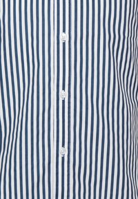 Koszulka typu button-up w paski z naprzemiennie ułożonymi niebieskimi i białymi pionowymi paskami, z białymi guzikami i gładką teksturą materiału.
