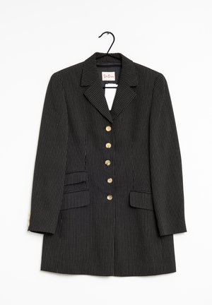 Blazer negro con rayas finas, con cinco botones delanteros y dos bolsillos con solapa colgado de un gancho sobre un fondo blanco.