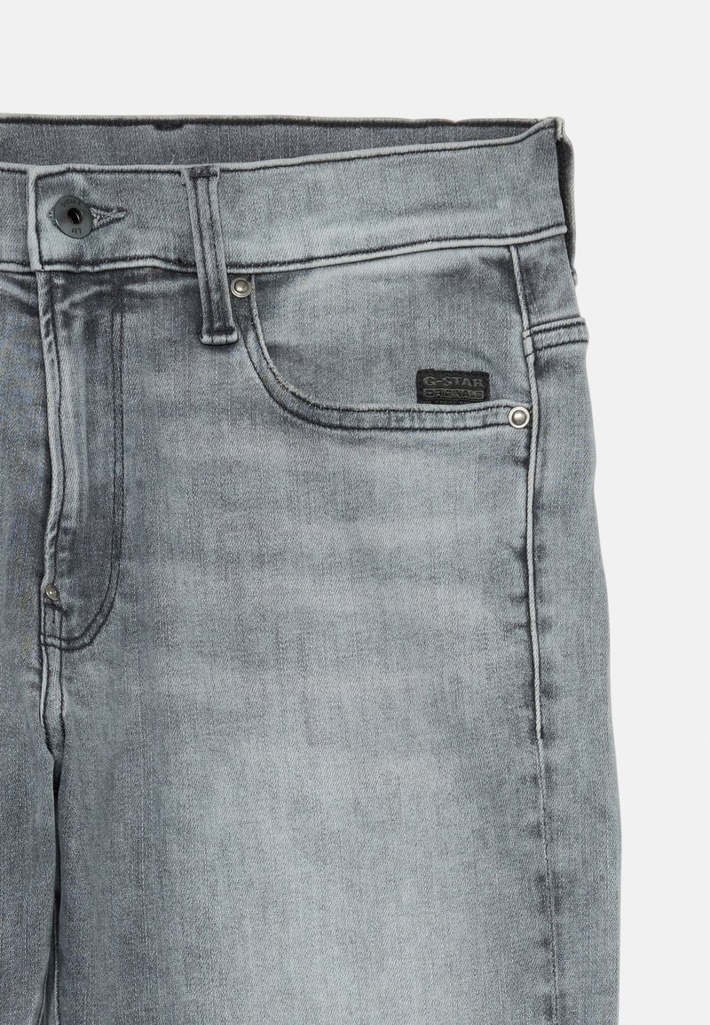 Jean en denim gris avec une texture lisse, dotée d'une poche avant, d'une fermeture à bouton en métal et d'une étiquette noire G-Star Originals sur la ceinture.
