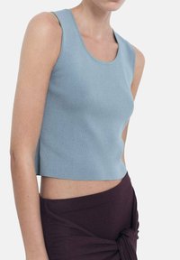 Světle modrý bezramínkový crop top vyrobený z ribbed materiálu, s kulatým výstřihem a přiléhavým střihem. Kombinováno s tmavě fialovou zavinovací sukní.