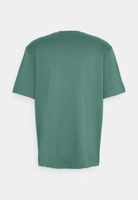 T-shirt à manches courtes dans un vert très doux, confectionné en coton doux. Design à col rond avec une texture lisse et une coupe décontractée. Vue arrière visible.