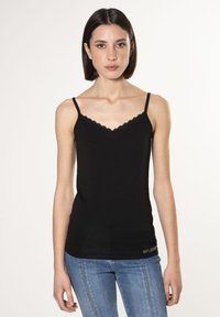 Camisola nera con scollo a V e bordo in pizzo, dotata di spalline sottili e regolabili. Tessuto morbido e design aderente, abbinata a jeans blu.