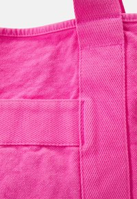 Różowa torba nożna z płótna o fakturowanej powierzchni, z ukośnymi wzorami tkanymi i mocnym szyciem uchwytów oraz dolnego szwu.