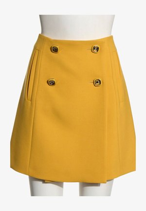 Jupe trapèze jaune moutarde avec deux poches verticales et quatre boutons carrés décoratifs sur la partie avant de la taille.