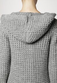 Maglione grigio lavorato a maglia con un cappuccio prominente, caratterizzato da un motivo testurizzato e dettagli di cucitura visibili sul retro.