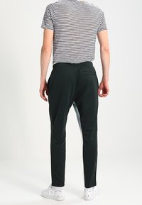 Mörkgröna träningsbyxor med slim fit och en bakficka, tillsammans med en randig t-shirt och vita sneakers.