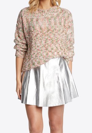 Kobieta ubrana w różowo-zielony dzianinowy sweter z podwiniętymi rękawami, zestawiony z błyszczącą srebrną plisowaną mini spódnicą, widoczny tułów.