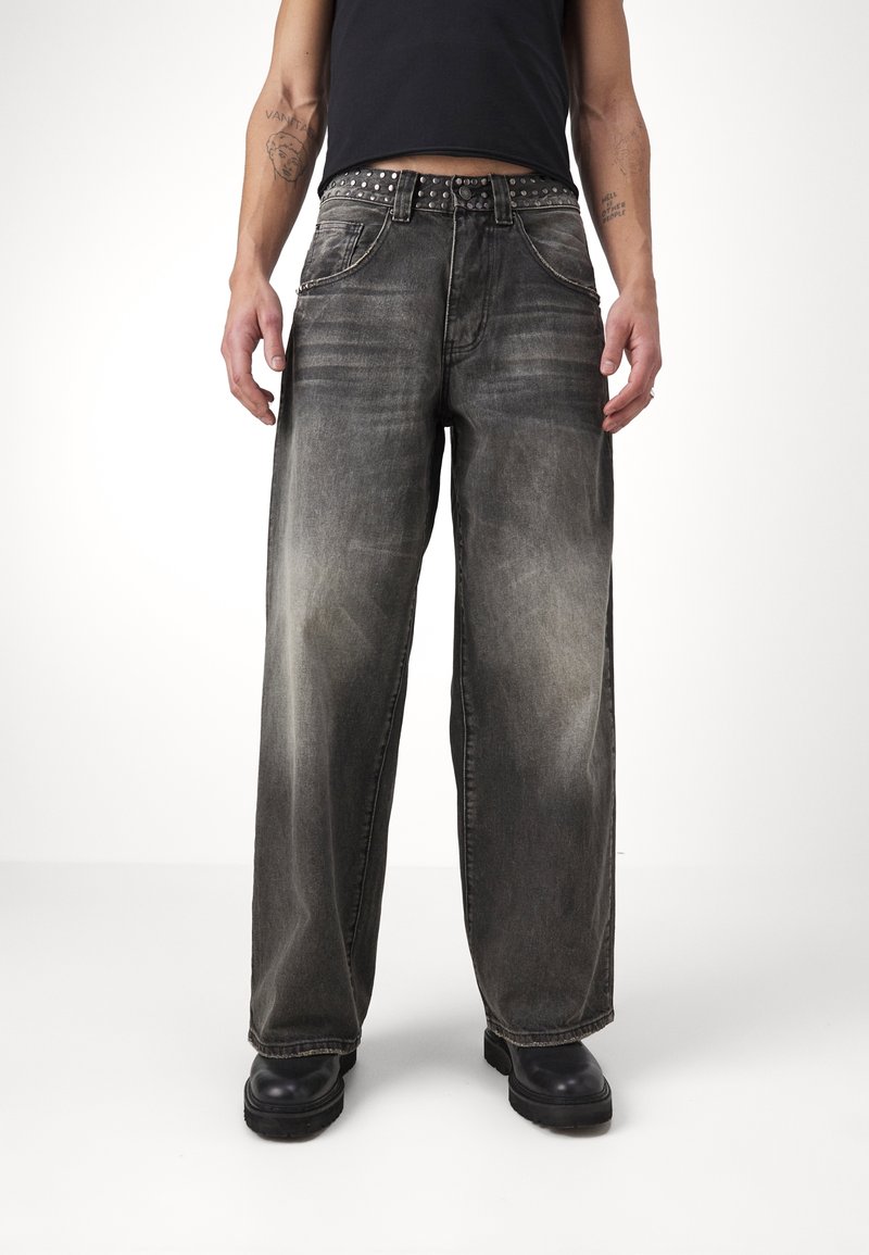 Grå vida jeans med en urtvättad finish och kontrasterande sömmar, kombinerat med ett nitarbälte. Svarta skor fulländar looken.