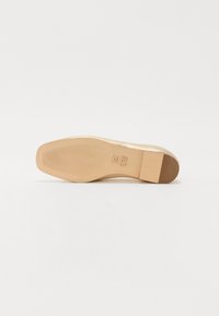 Semelle de chaussure plate beige avec une texture lisse, dotée d'un petit talon carré et d'un motif strié pour une meilleure adhérence. Marque imprimée sur la surface.