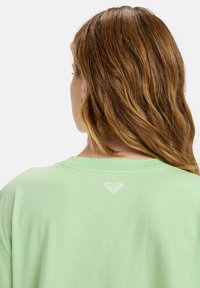 Mintgrünes T-Shirt mit Rundhalsausschnitt und kurzen Ärmeln. Mit einem subtilen Herzlogo in Weiß auf dem oberen Rücken. Aus weichem Baumwollmaterial.