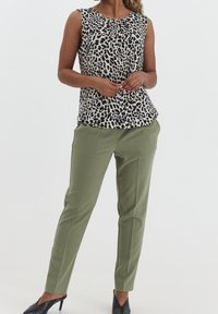 Débardeur sans manches beige avec imprimé léopard noir, associé à un pantalon olive ajusté. Des chaussures à talons noires complètent la tenue.