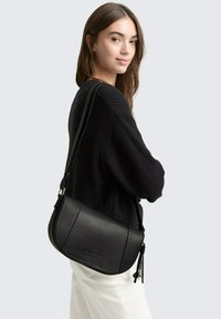 Borsa a tracolla in pelle nera con texture granulosa, forma curva e tracolla regolabile. Presenta una cerniera con dettaglio a nappina.