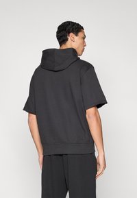 Μαύρο βαμβακερό φούτερ με κοντά μανίκια και μεγάλο κουκούλι, με άνετη εφαρμογή και εμφανή ραφή στο τελείωμα και τα μανίκια.