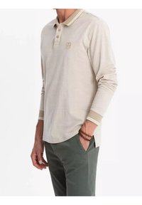 Polo beige à manches longues avec un col clair, une patte de boutonnage à trois boutons et des poignets rayés. Présente un logo brodé sur la poitrine.