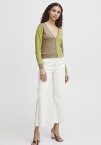 Cardigan color-block verde e marrone con scollatura a V e bottoni frontali, abbinato a pantaloni bianchi a gamba larga e sandali con tacco a blocco trasparente.