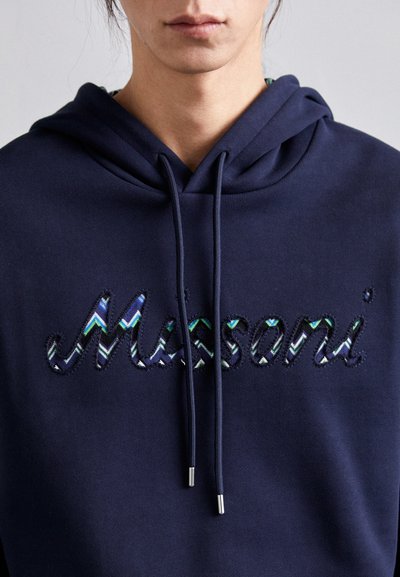 Sweatshirt azul-marinho com cordão. Apresenta a palavra "Missoni" em bordado zig-zag multicolorido. Textura de tecido suave, design casual.