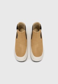 Botines de ante beige con paneles laterales de elastano y suela de goma blanca. Interior forrado con un material suave para mayor comodidad.