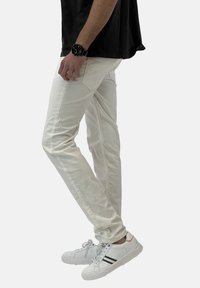 Jeans bianchi in cotone con una vestibilità slim, caratterizzati da dettagli di cucitura discreti. Abbinati a sneaker bianche con strisce nere e un accento arancione.