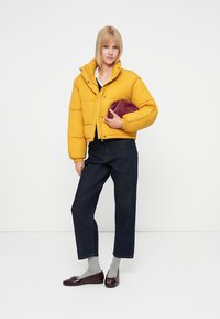 Kollane puffjakker, millel on lühendatud disain, tumesinised teksad, hallid sokid ja burboonia punane käekott. Läikivad burboonia punased loafers'id viivad look'i viimistlema.