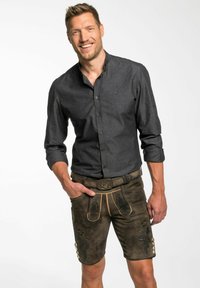 Dunkelgrau gestreifte Hemd kombiniert mit braunen Leder-Shorts, die dekorative Akzente, goldene Nähte und silberne Knöpfe an der Seite aufweisen.