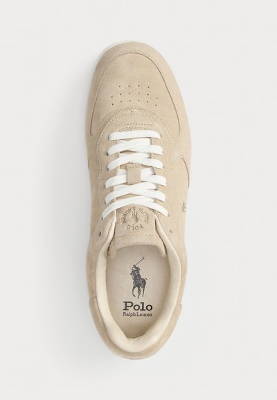 Baskets en suède beige avec des lacets blancs, embout perforé et logo imprimé sur la semelle intérieure. Texture douce et forme arrondie.