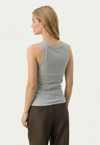 Harmaa ribbattu tank top, jossa on pyöreä pääntie, hihattomat mallit ja tiukka muoto. Yhdistetty ruskeisiin räätälöityihin housuihin.