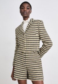 Svart, vit och guld rutig blazer och shorts-set med en strukturerad design och beskuren passform; har knappstängning och textilstruktur.