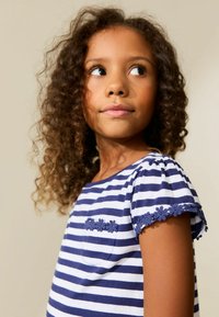 T-shirt rayé bleu et blanc avec des manches courtes à volants, comprenant un accent en dentelle florale sur les manches et une petite poche poitrine.