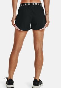 Svarta träningsshorts med rosa sidopaneler och ett brett elastiskt midjeband med text. Materialet verkar lätt och har en slät textur.