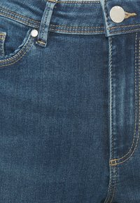 Mörkblå denimjeans med en slät yta, med kopparstygn, femficksdesign och en metalldekor på midjan.